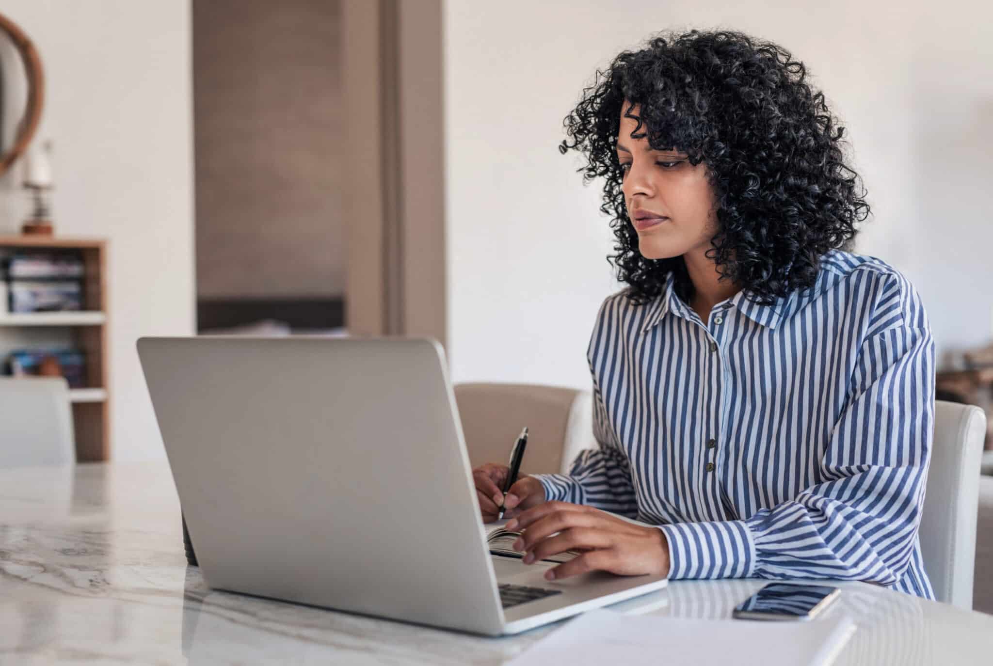 Professional woman working at a laptop while taking notes at her desk